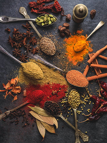 Vibrant array of spices including turmeric, cumin, and chili arranged on a dark surface. HD phone wallpaper