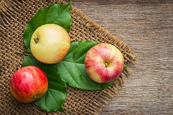 Three ripe apples on leaves over a rustic wooden background, emphasizing freshness and nutrition. HD wallpaper