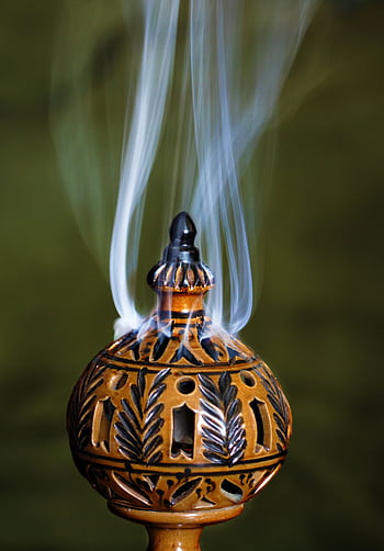 Elegant ceramic incense burner with intricate design and smoke rising against a green background. HD phone wallpaper