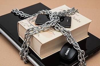 Chain-locked book, , and laptop symbolizing digital and intellectual security. HD wallpaper
