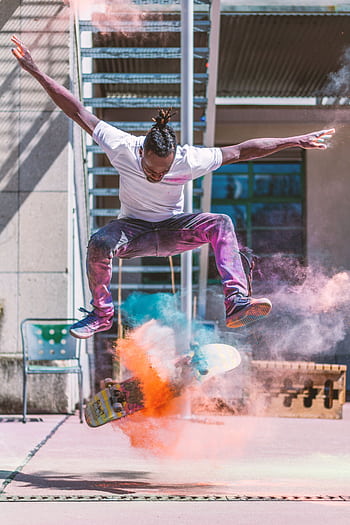 A young man performs a skateboarding trick with colorful smoke effects outdoors. HD phone wallpaper