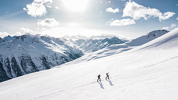 Two skiers climbing a sunlit snowy mountain slope in Ischgl, Austria, during winter. HD wallpaper
