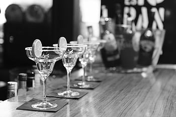 Monochrome margarita glasses on a bar counter with lemon slices, creating an elegant atmosphere. HD wallpaper