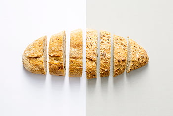 Freshly baked whole wheat bread sliced on a white background, showcasing its homemade texture. HD wallpaper