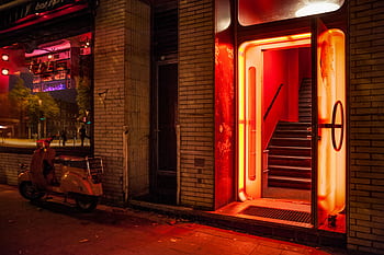 Illuminated entrance of a nightclub with neon red lights and a vintage scooter. HD wallpaper