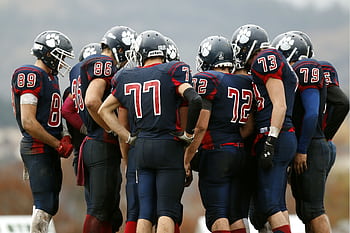 American football players in a huddle planning their next move on a grassy field. HD wallpaper