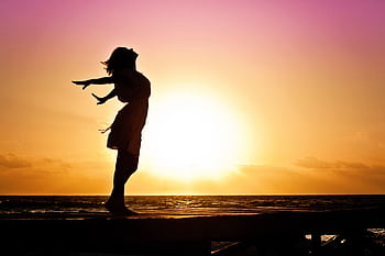 Silhouette of a woman at the beach with arms outstretched against a vibrant sunset backdrop. HD wallpaper