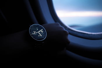 A smartwatch on a wrist shown against an airplane window view during flight. HD wallpaper