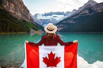 Woman holding a Canadian flag at stunning Lake Louise, Alberta, embracing nature and patriotism. HD wallpaper