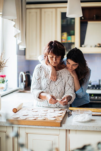 A mother and daughter bond while preparing traditional dumplings in a cozy kitchen setting. HD phone wallpaper