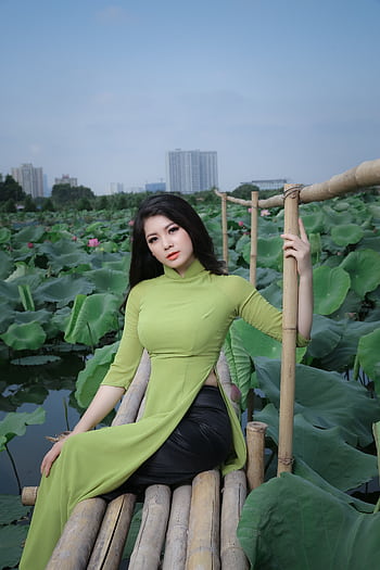 Asian woman in green ao dai posing by lotus pond, showcasing cultural fashion and natural beauty. HD phone wallpaper
