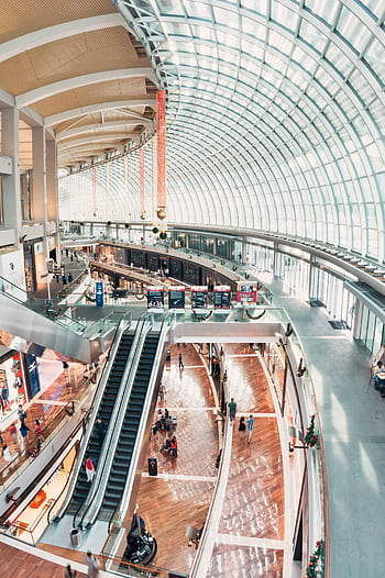 Spacious indoor shopping mall with glass ceilings and a modern design, including escalators and shops. HD phone wallpaper