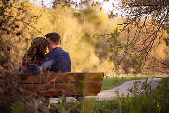 A couple enjoying a cozy moment on a park bench surrounded by nature. HD wallpaper