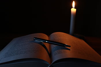 An open book and pen on a desk illuminated by candlelight, creating a tranquil study atmosphere. HD wallpaper