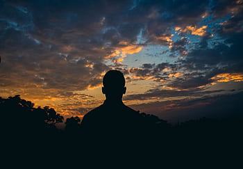 Silhouette of a man against a colorful sunset sky with clouds. Perfect for serene, introspective themes. HD wallpaper