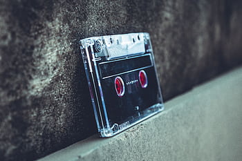 Close-up of a vintage cassette tape resting on a concrete surface, highlighting nostalgic audio technology. HD wallpaper