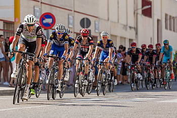Dynamic of professional cyclists racing on a city street, showcasing speed and athleticism. HD wallpaper