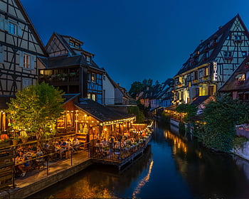 Nighttime view of Colmar's timbered houses and canal-side dining, beautifully illuminated. HD wallpaper