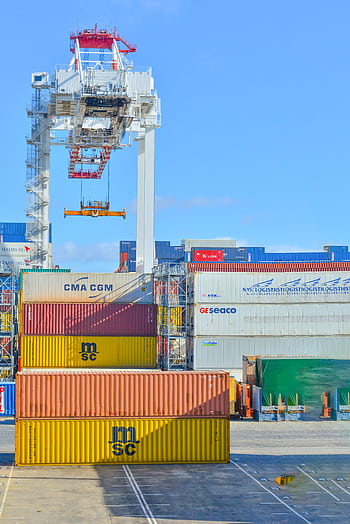 Stacked cargo containers in a sunny port industrial setting with crane. HD phone wallpaper