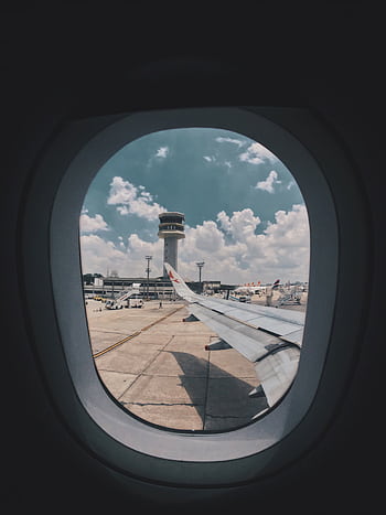 Airplane wing view through window showing airport control tower and tarmac. HD phone wallpaper