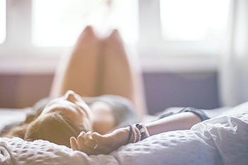 A woman lying on a bed in a peaceful, sunlit room, conveying relaxation. HD wallpaper