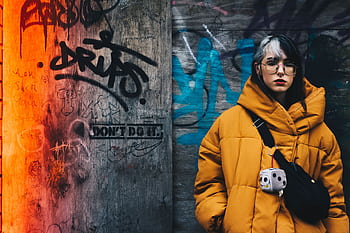 Young woman in yellow winter jacket against vibrant graffiti wall, conveying urban street style. HD wallpaper