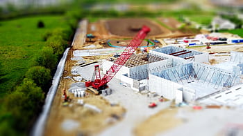 Aerial view of a construction site with a red crane amidst green fields and concrete buildings. HD wallpaper