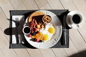A delicious breakfast spread featuring eggs, bacon, fruit, and coffee on a sunlit table. HD wallpaper