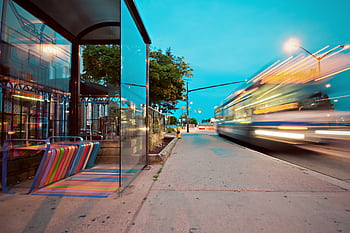 Colorful city bus stop with vibrant benches, blurred motion of a passing bus at dusk. HD wallpaper