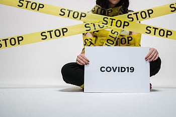 A woman holding a COVID-19 sign surrounded by yellow stop tape, conveying caution and awareness. HD wallpaper