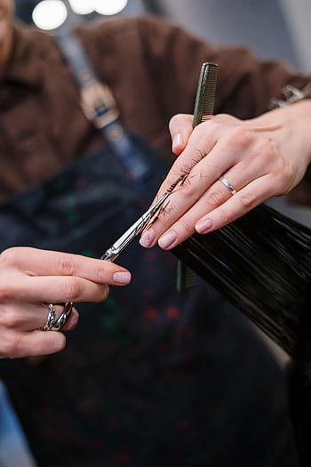 A professional hairstylist cutting hair in a salon, showcasing skilled technique. HD phone wallpaper