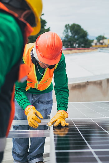 Worker in safety gear installing solar panels on a rooftop. HD phone wallpaper
