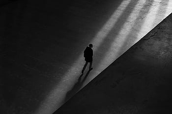 Black and white of a man walking through shadows on a deserted pavement, creating a moody silhouette. HD wallpaper