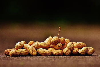 Close-up of a pile of peanuts in shells on a wooden surface. Ideal for food and nutrition themes. HD wallpaper