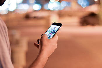 A close-up of a person using a smart outdoors at night, with blurred bokeh lights in the background. HD wallpaper