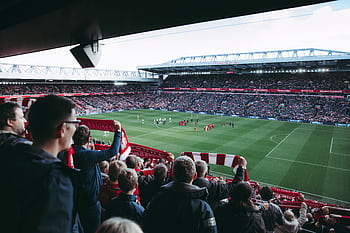 Fans cheer as players take the field at a vibrant football stadium, creating an electric atmosphere. HD wallpaper