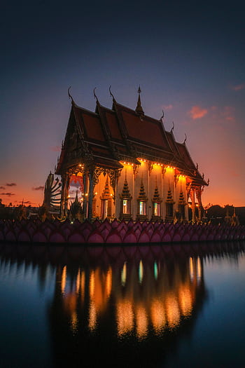 A stunning shot of a beautifully lit Thai temple at sunset, reflecting in the serene water. HD phone wallpaper