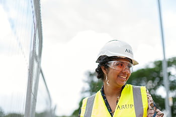 Smiling female engineer in protective gear at an outdoor construction site. HD wallpaper