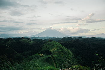 Breathtaking aerial view of Mayon Volcano surrounded by lush hills under a cloudy sky. HD wallpaper