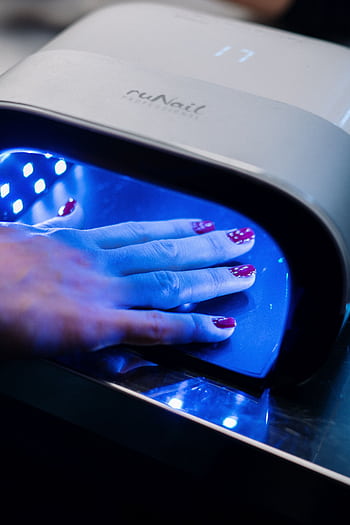 A hand with red nail art curing under a UV lamp in a professional nail salon. HD phone wallpaper