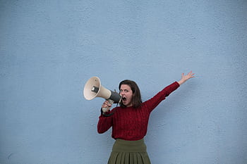 A woman expressing loudly with a mega against a blue wall, capturing energy and expression. HD wallpaper