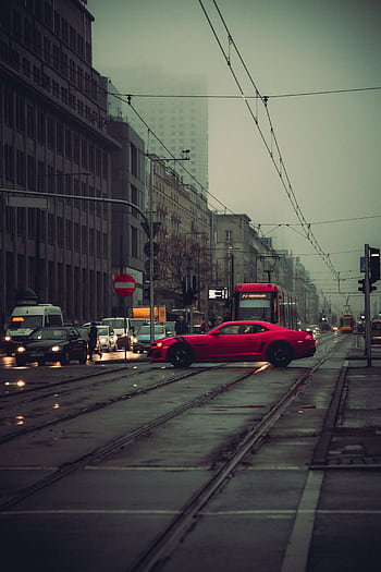 A red car on a rainy street in Warsaw, capturing urban life. HD phone wallpaper