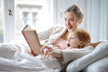 Mother and daughter bonding during a cozy storytime session in bed. HD wallpaper