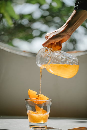 Hand pouring fresh orange juice into a glass, capturing a vibrant summer moment. HD phone wallpaper