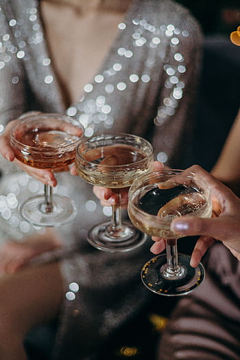Three people clinking glasses filled with cocktails during a celebration with shimmering attire. HD phone wallpaper