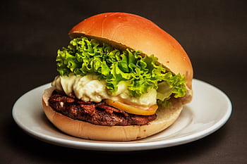 Close-up of a gourmet cheeseburger with fresh lettuce, mayonnaise, and beef patty on a white plate. HD wallpaper