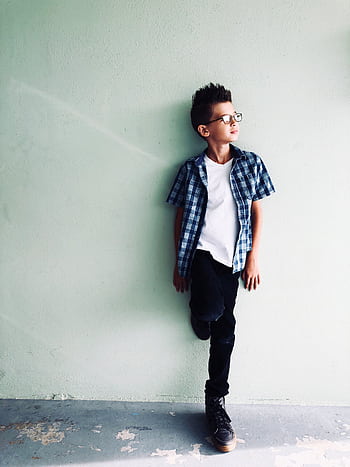 Fashionable young boy wearing plaid shirt, posing against a light wall, exuding stylish confidence. HD phone wallpaper