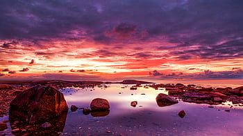 Vibrant sunset reflecting over rocky seashore, dramatic clouds and calm water create que scenery. HD wallpaper