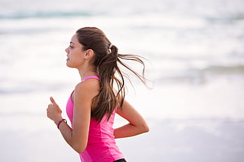 Side view of a young woman jogging on a beach wearing pink active wear. HD wallpaper