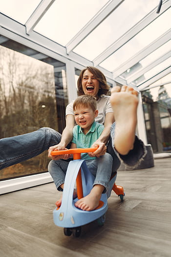 A joyful moment of a mother and son playing indoors on a toy car, showcasing love and happiness. HD phone wallpaper